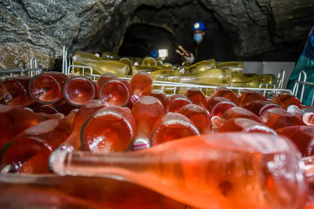 Bottiglie di birra in affinamento all’interno di una galleria mineraria, con operatori sullo sfondo.