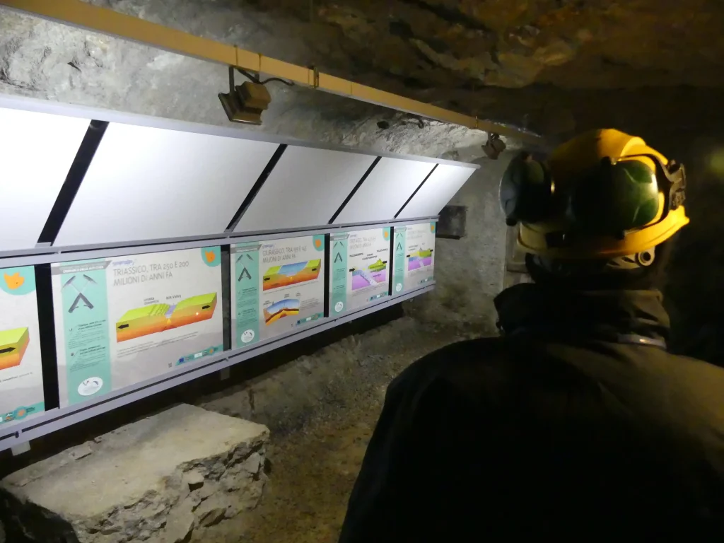 Visitatore osserva pannelli didattici sulla tettonica a placche installati all'interno di una galleria mineraria.